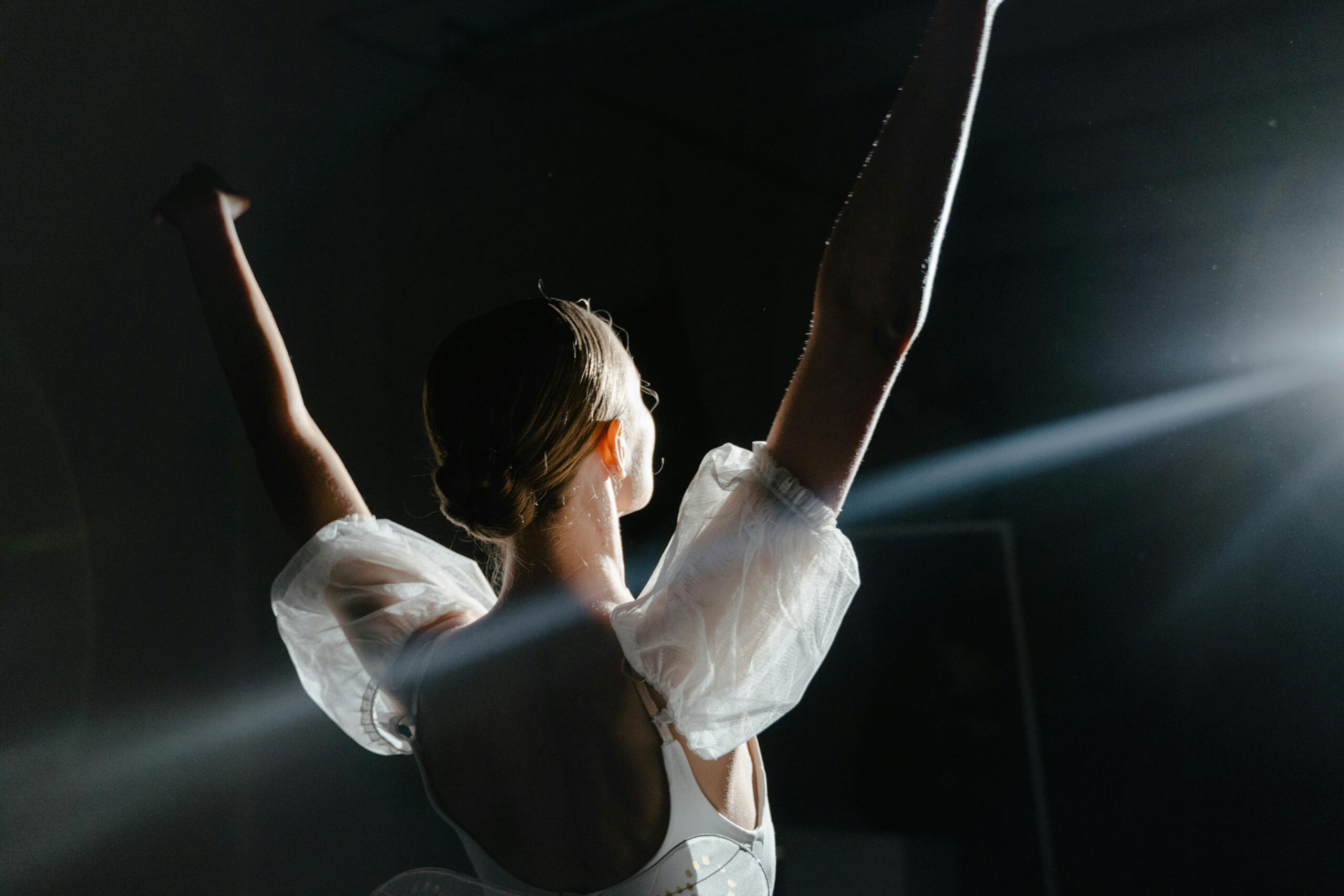 Programs A professional ballerina in a white dress performs gracefully under dramatic stage lighting.