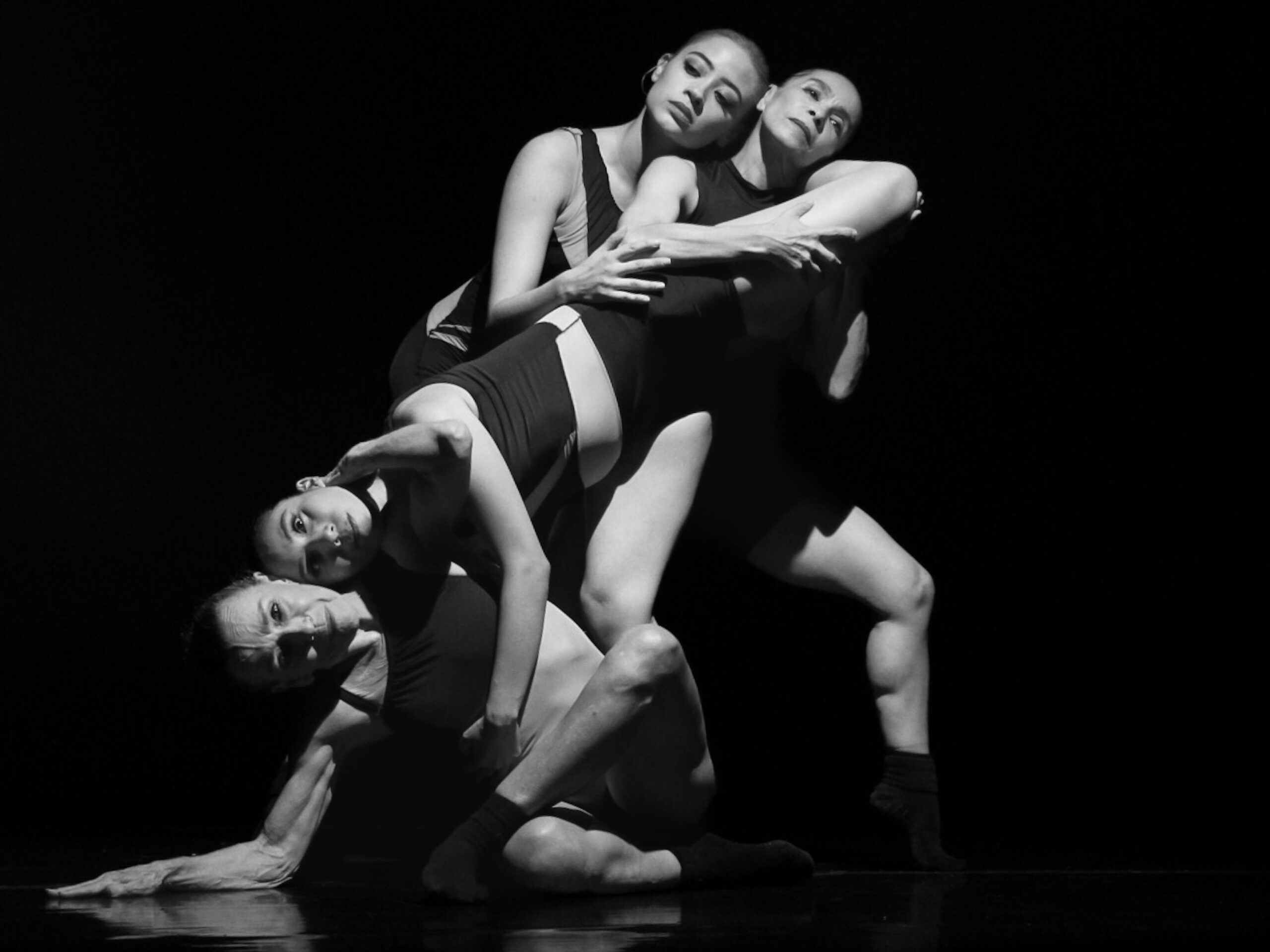 Four dancers in a dynamic modern dance pose in black and white.